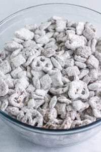 Glass bowl piled high with finished Best Sweet Chex Mix Recipe Muddy Buddy fully coated in chocolate and powdered sugar ready to serve.