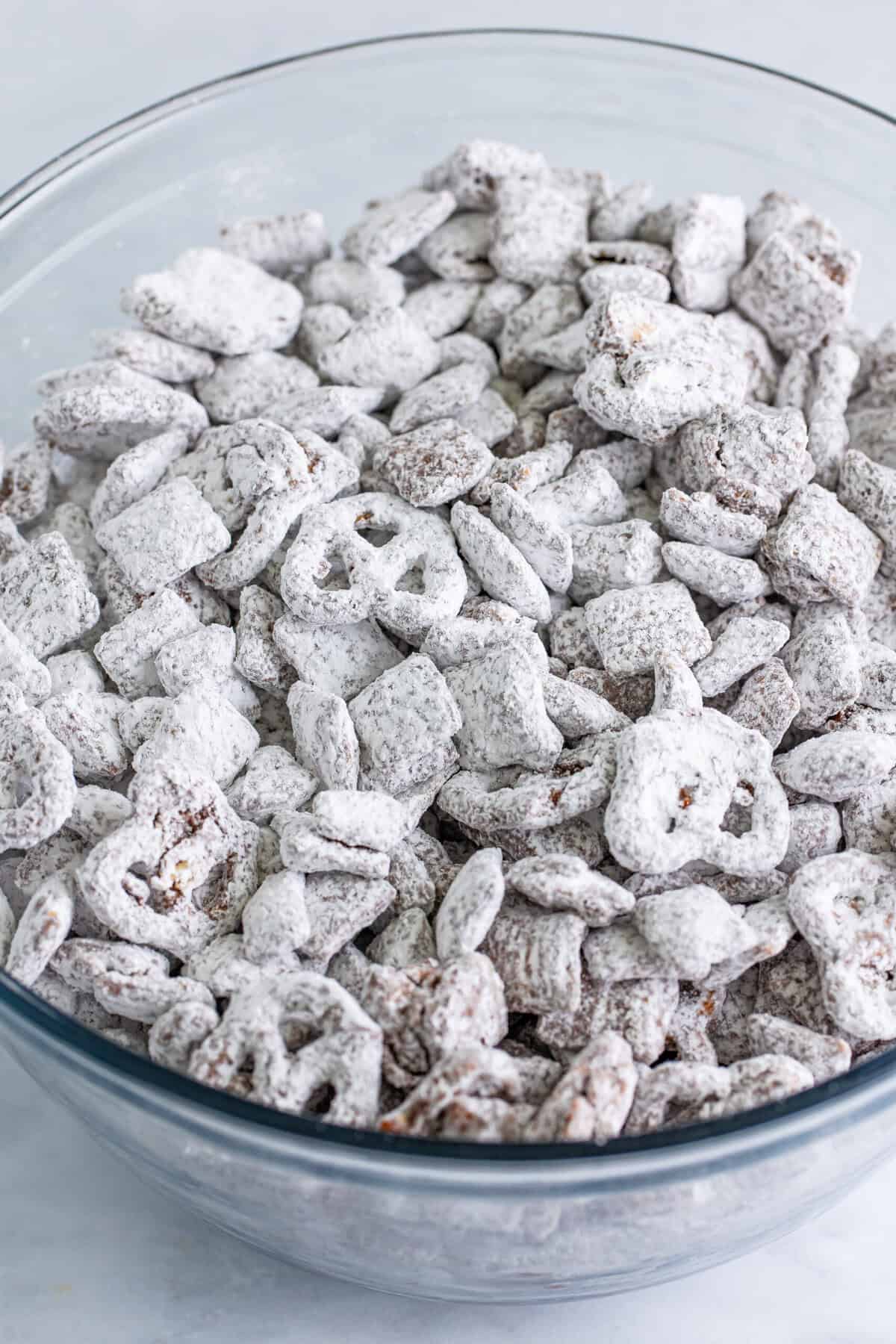 Finished puppy chow muddy buddies coated in powdered sugar in a glass bowl.