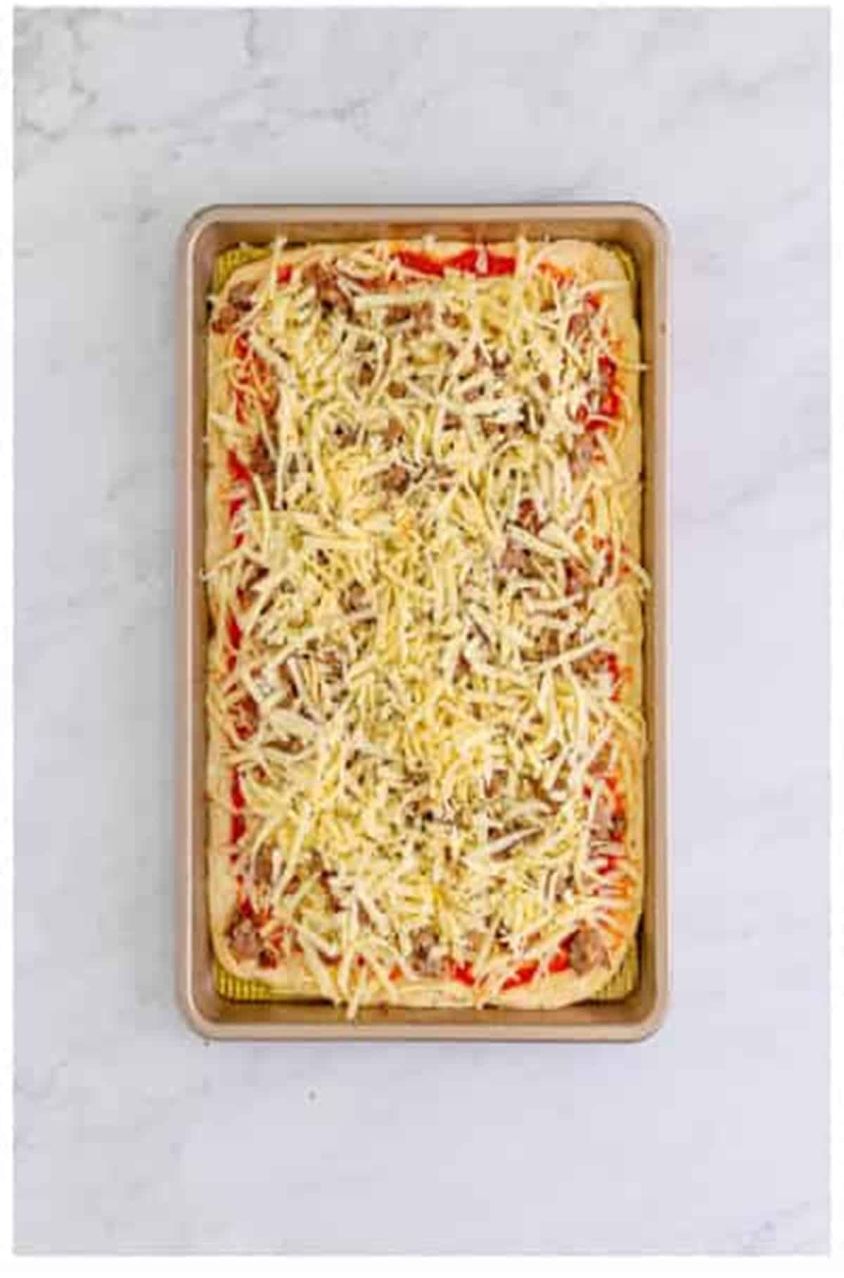 Cooked Italian sausage crumbles topped with the remaining shredded mozzarella for The Best Sheet Pan Pizza Recipe.