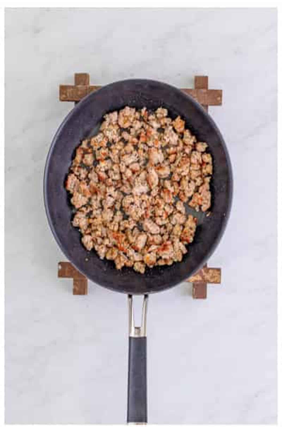 Homemade Italian sausage crumbling and browning in a black skillet for The Best Sheet Pan Pizza Recipe.