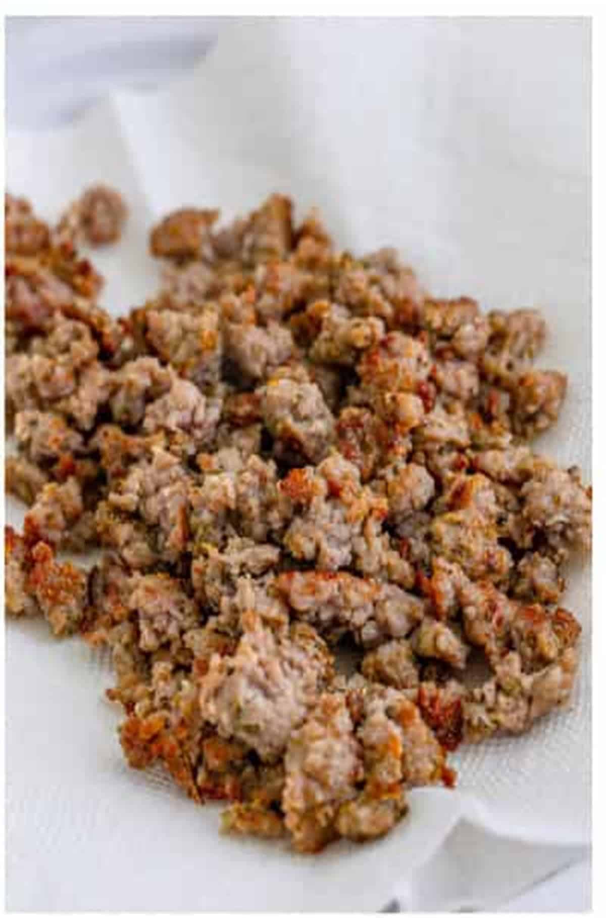 Cooked Italian sausage crumbles draining on a paper-towel-lined plate for The Best Sheet Pan Pizza Recipe.