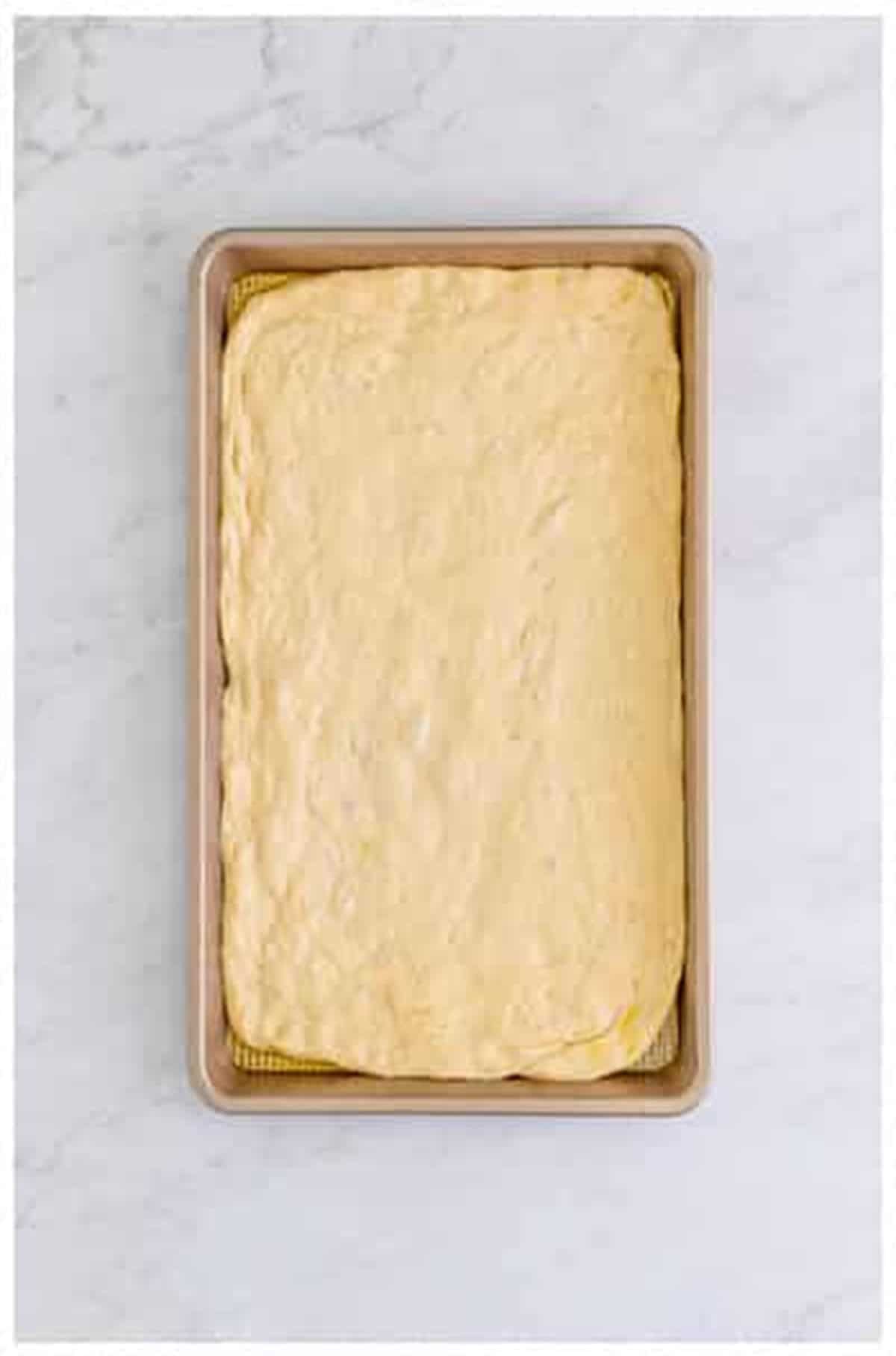 Pizza dough stretched out to fill a 9x13 rimmed sheet pan in an even layer for The Best Sheet Pan Pizza Recipe.