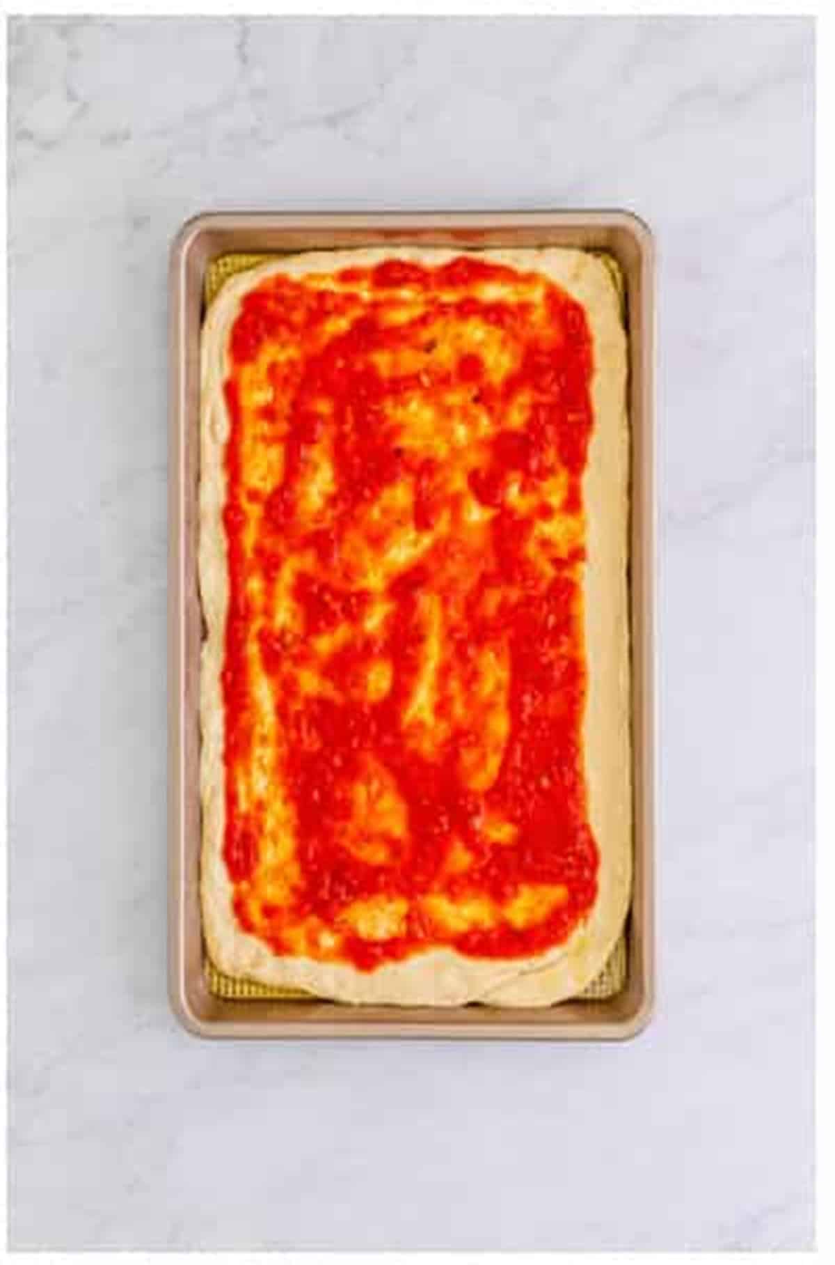 Pizza sauce spread evenly over stretched dough leaving a half-inch border for The Best Sheet Pan Pizza Recipe.