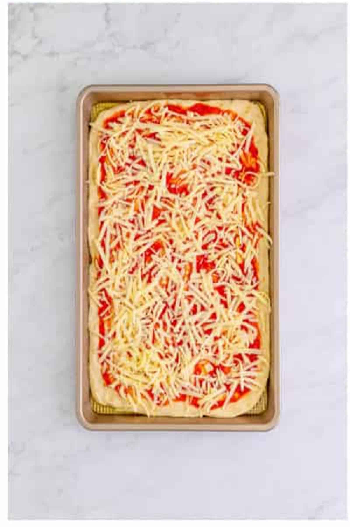 First half of shredded mozzarella cheese spread over the pizza sauce for The Best Sheet Pan Pizza Recipe.
