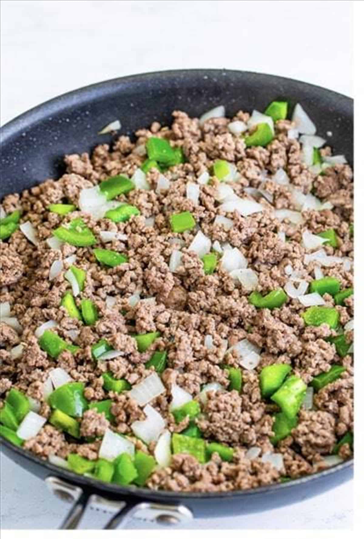 Browned ground beef with onion and green pepper in a skillet for award winning chili.