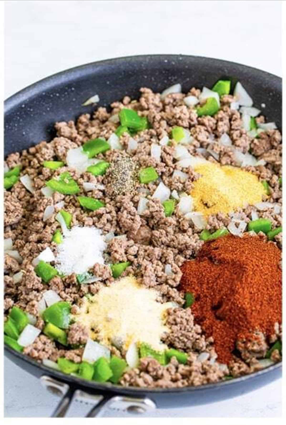 Chili powder and seasonings added to the browned beef in a skillet.