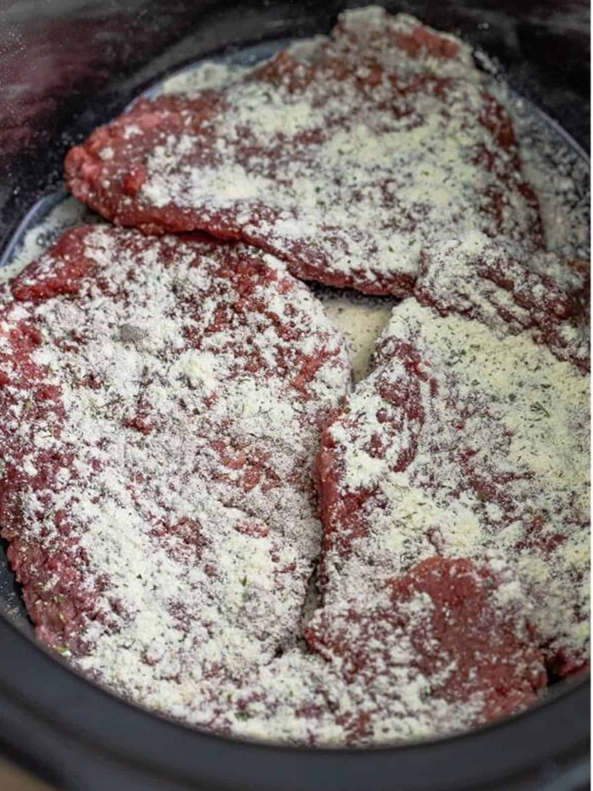 Cube steaks layered in a slow cooker and sprinkled with au jus seasoning for Slow Cooker Cube Steak.