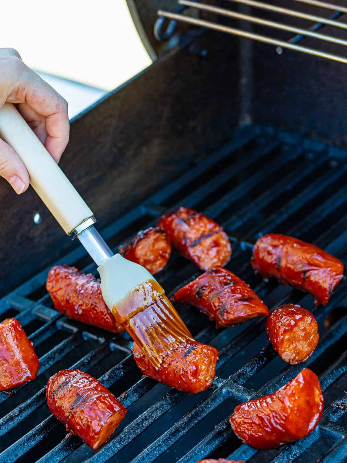 Basting smoked kielbasa with BBQ sauce on the grill.