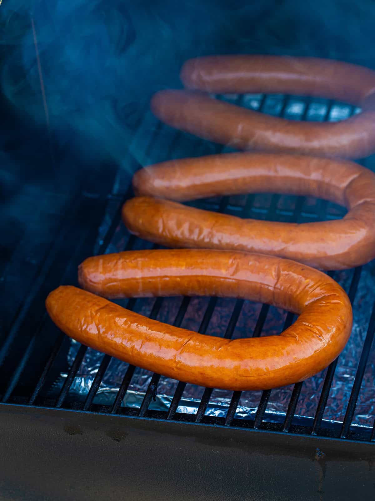 Kielbasa coils smoking on a smoker rack.