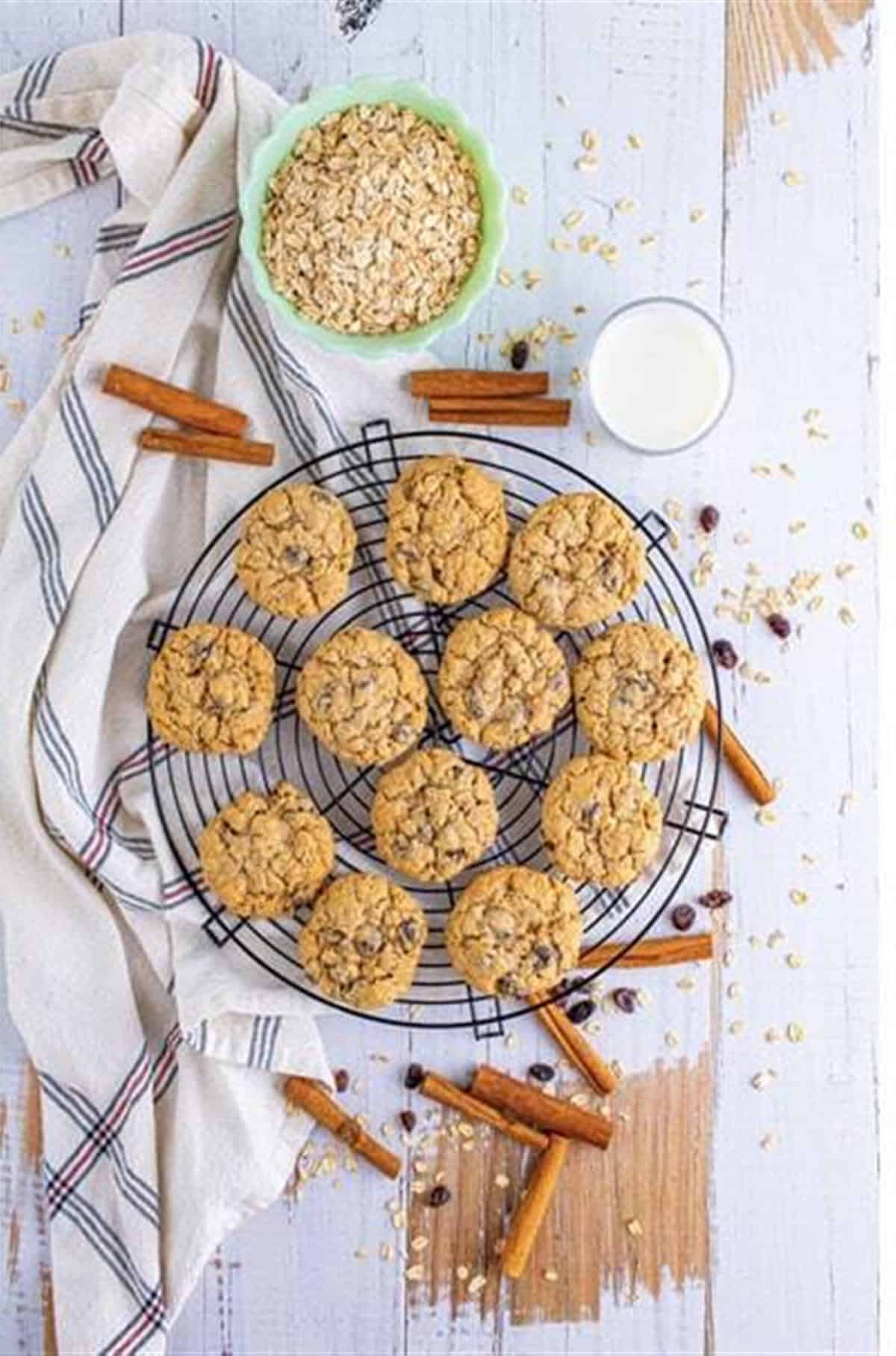 Soft Chewy Oatmeal Raisin Cookies on a wire cooling rack with cinnamon sticks, oats, and a glass of milk.