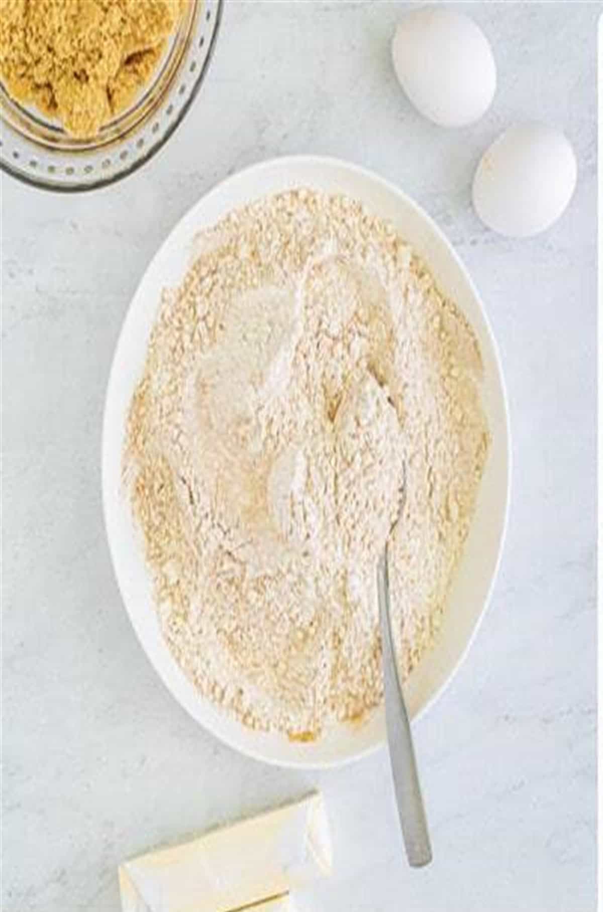 Flour, oats, cinnamon, and spices in a bowl with eggs and butter nearby for Soft Chewy Oatmeal Raisin Cookies.