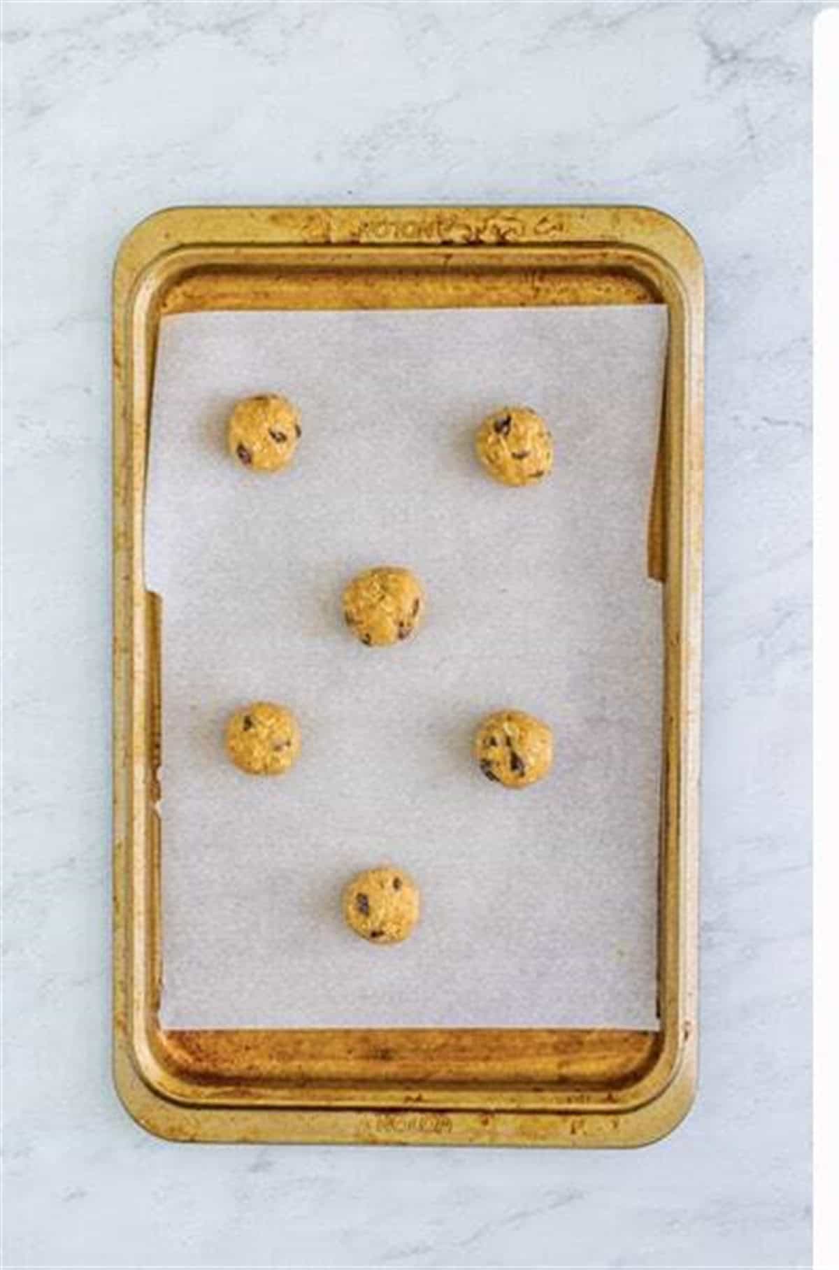 Two-tablespoon scoops of oatmeal raisin cookie dough on a parchment-lined baking sheet ready for the oven.