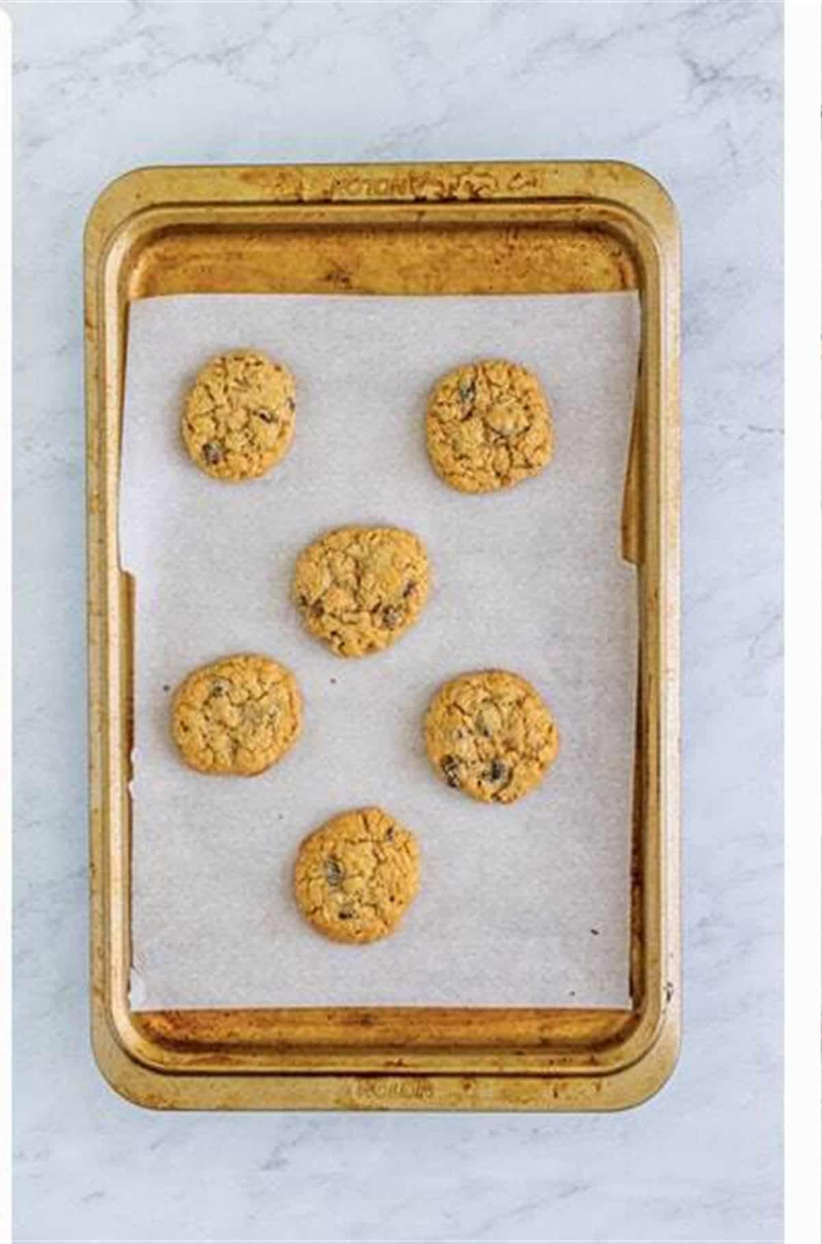 Soft Chewy Oatmeal Raisin Cookies fresh from the oven on a parchment-lined baking sheet with golden edges.