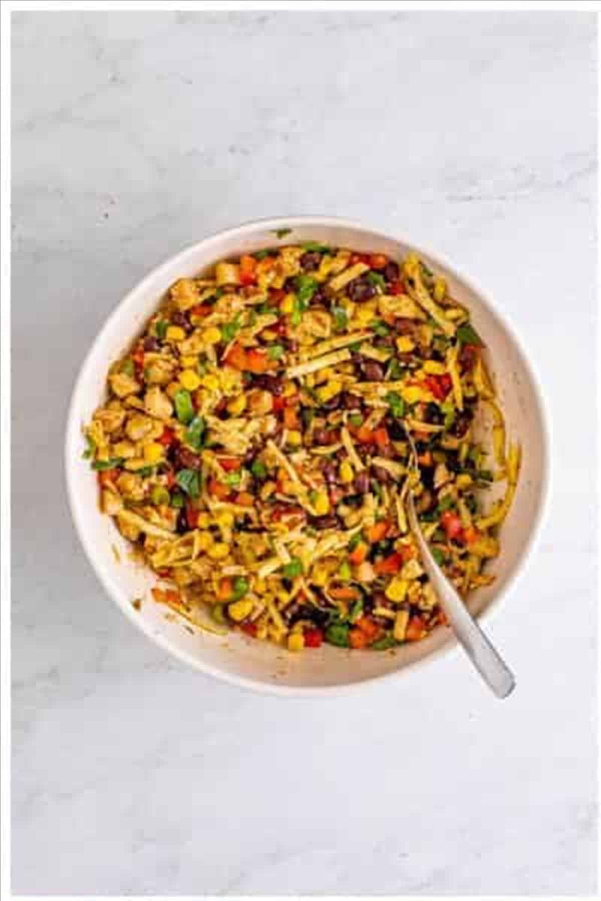 Cooked chicken, shredded cheese, black beans, corn, red bell pepper, scallions, jalapenos, and spices mixed together in a large white bowl for Southwest Egg Rolls filling.