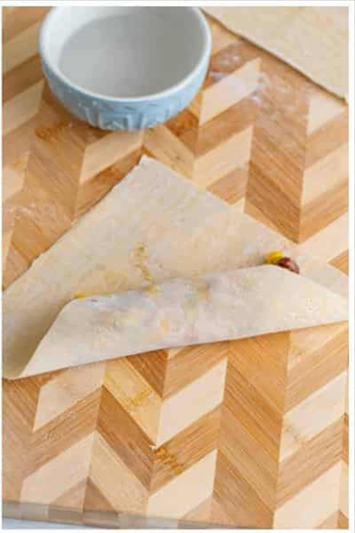 Egg roll wrapper folded over and partially rolled around the Southwest filling on a wooden cutting board.