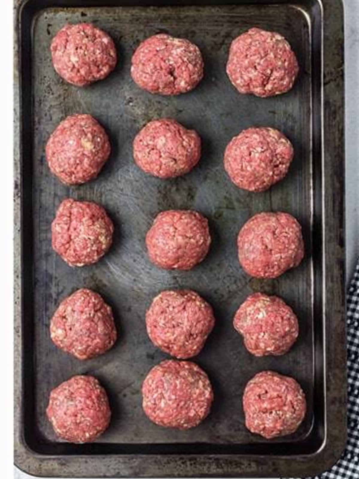 Raw rolled meatballs on a sheet tray ready to bake for Spaghetti and Meatballs.