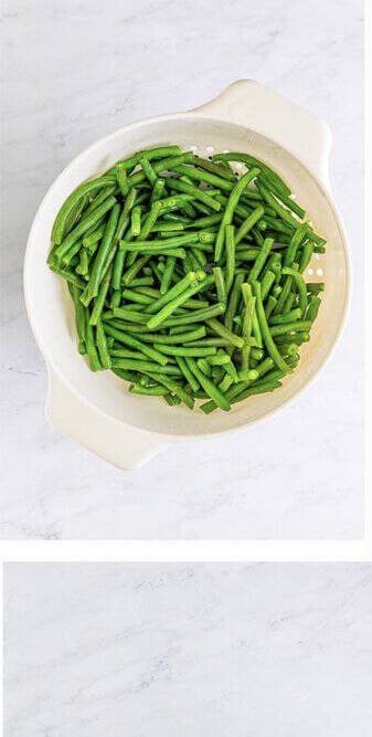Blanched green beans drained in a colander, ice cold and crisp, ready for the Cold Green Bean Salad.