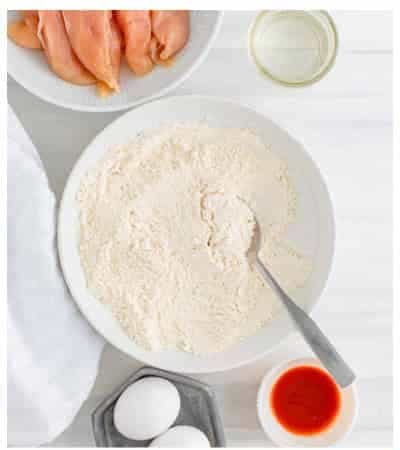 Adding seasoning spices into the seasoned flour dredge bowl for Air Fryer Buffalo Chicken Tenders.