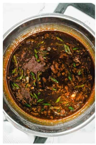 Whisking soy sauce, brown sugar, sesame oil, garlic, ginger, and scallions in a pan for Asian shrimp marinade.