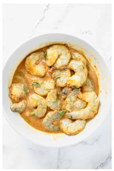 Raw peeled shrimp tossed in Asian marinade to coat in a clear glass bowl.