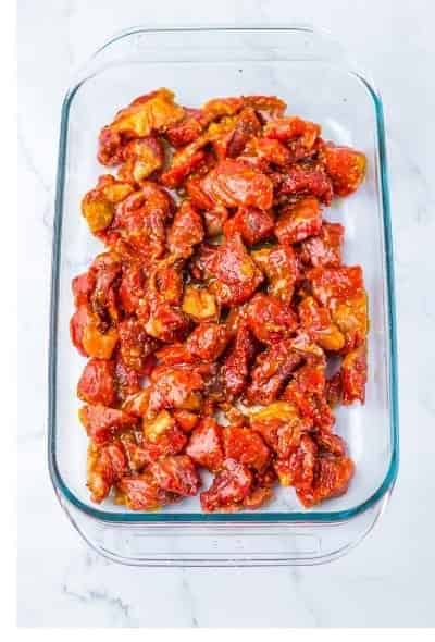 Seasoned chuck roast cubes spread in a single layer in a glass baking dish for the first oven roast.