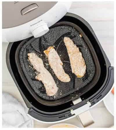 Breaded chicken tenders arranged in a single layer in the air fryer basket ready to cook.