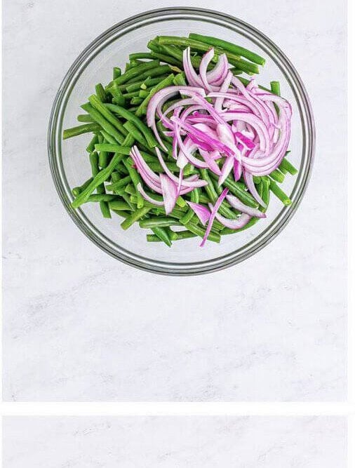 Blanched green beans and thinly sliced red onion in a large mixing bowl before tossing with vinaigrette.
