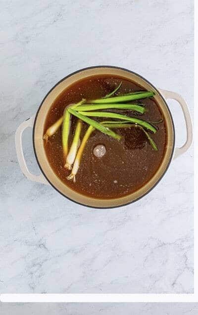 Building the Wonton Soup broth by adding chicken stock, scallions, ginger, garlic, and soy sauce to a Dutch oven.