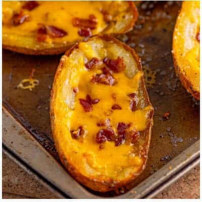 Adding shredded sharp cheddar and crispy bacon bits to the crisped potato skins for the final cheese melt.