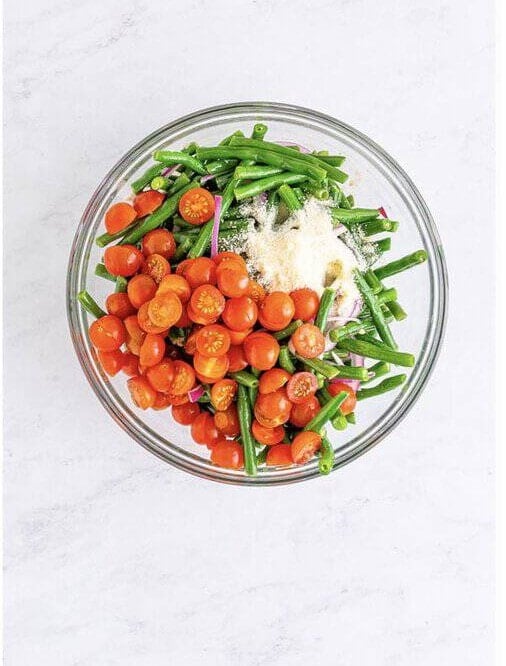 Halved cherry tomatoes and grated parmesan added to the dressed green beans and red onion for Cold Green Bean Salad Recipe.