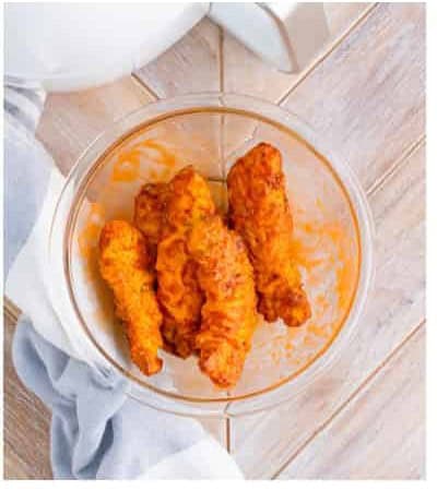 Fried chicken tenders tossed in buffalo sauce in a clear glass bowl for the final coating.