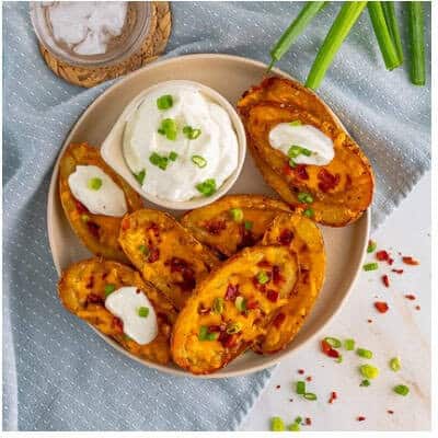 Finished Loaded Potato Skins served with a small bowl of sour cream and scallion garnish for dipping.
