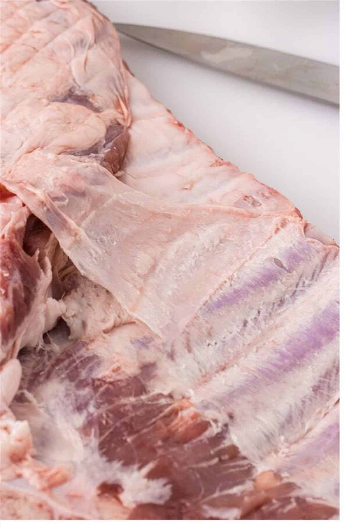 Raw St. Louis ribs with membrane being removed on a baking sheet.