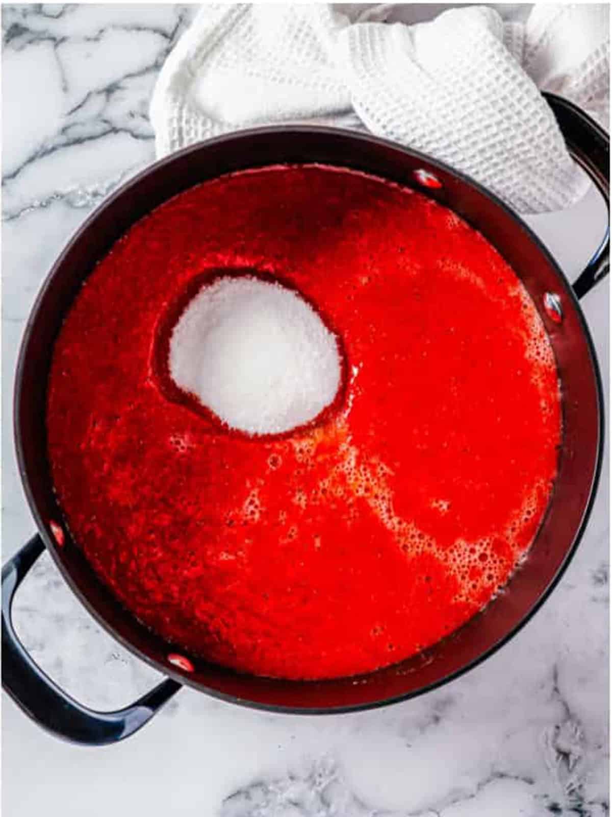 Adding sugar to the strawberry puree in a pot to cook down.