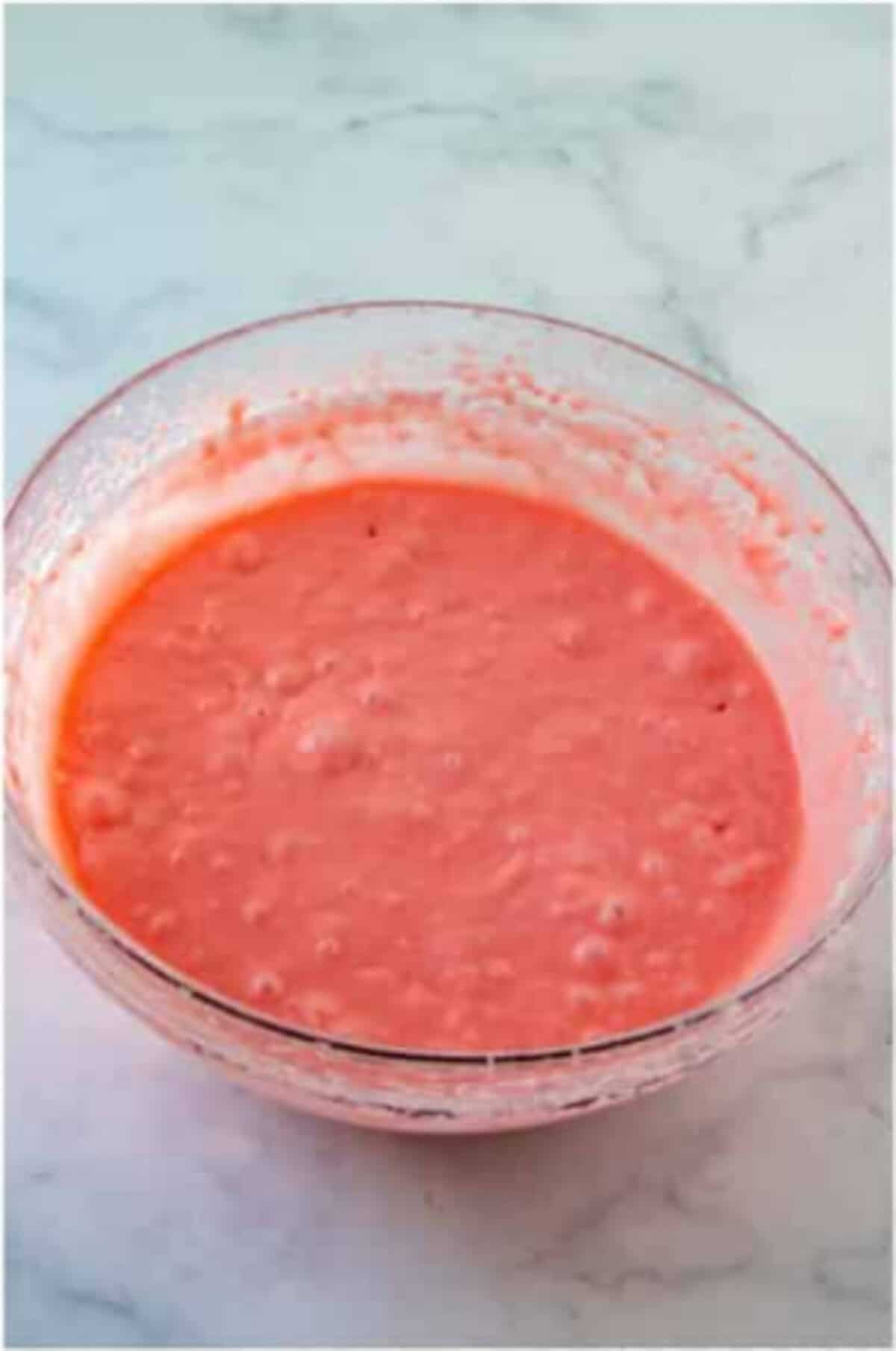 Pink strawberry cake batter mixed in a glass bowl.