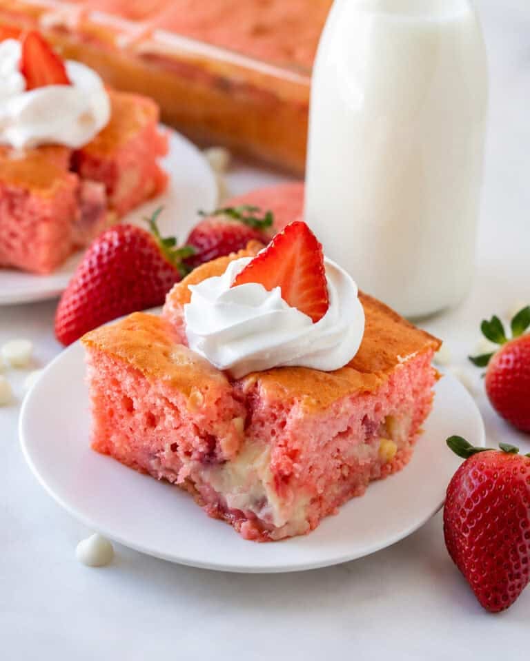 Slice of Strawberry Earthquake Cake on a plate with cheesecake swirl visible and fresh strawberries on top.