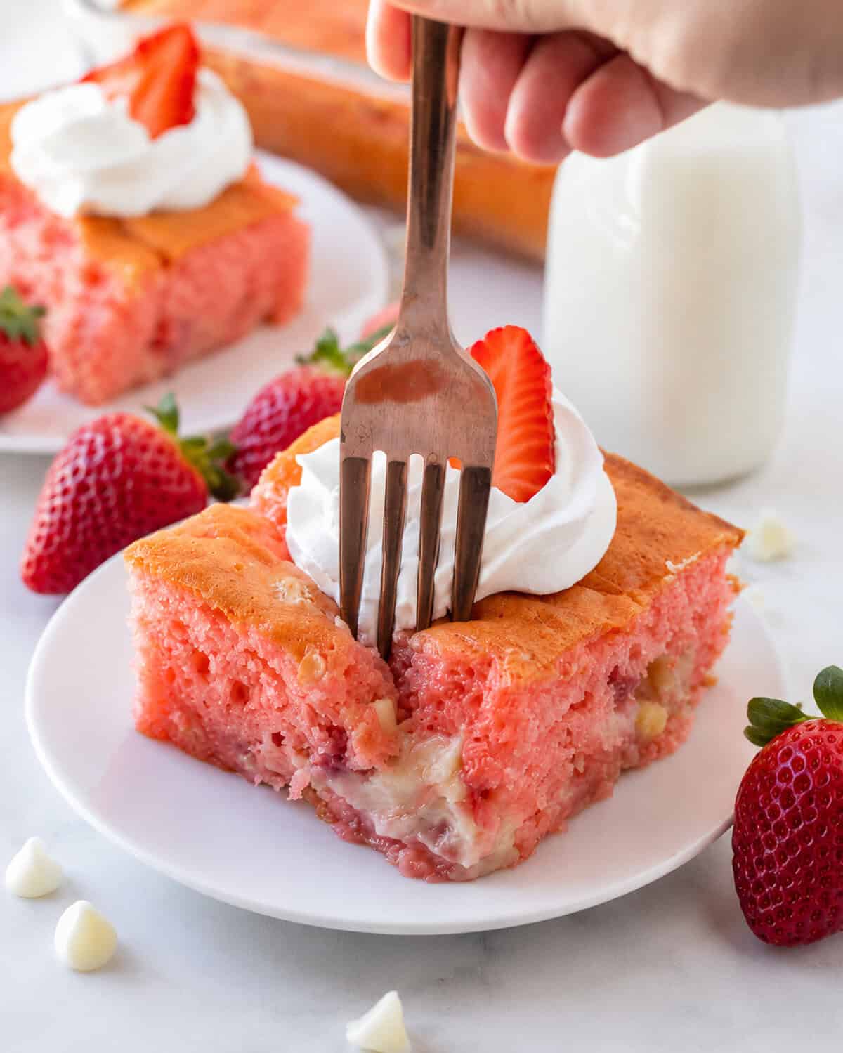 A fork taking a bite of a slice of strawberry earthquake cake.