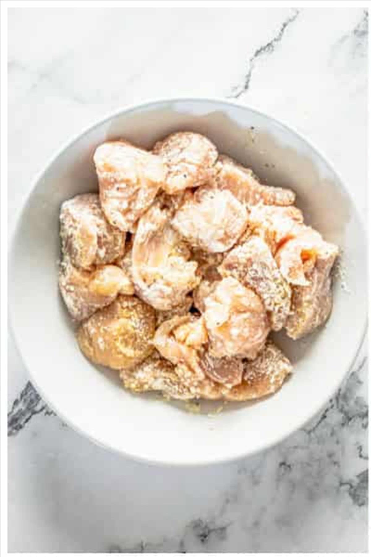 Diced chicken tossed with cornstarch and seasonings in a white bowl for sweet and sour chicken.