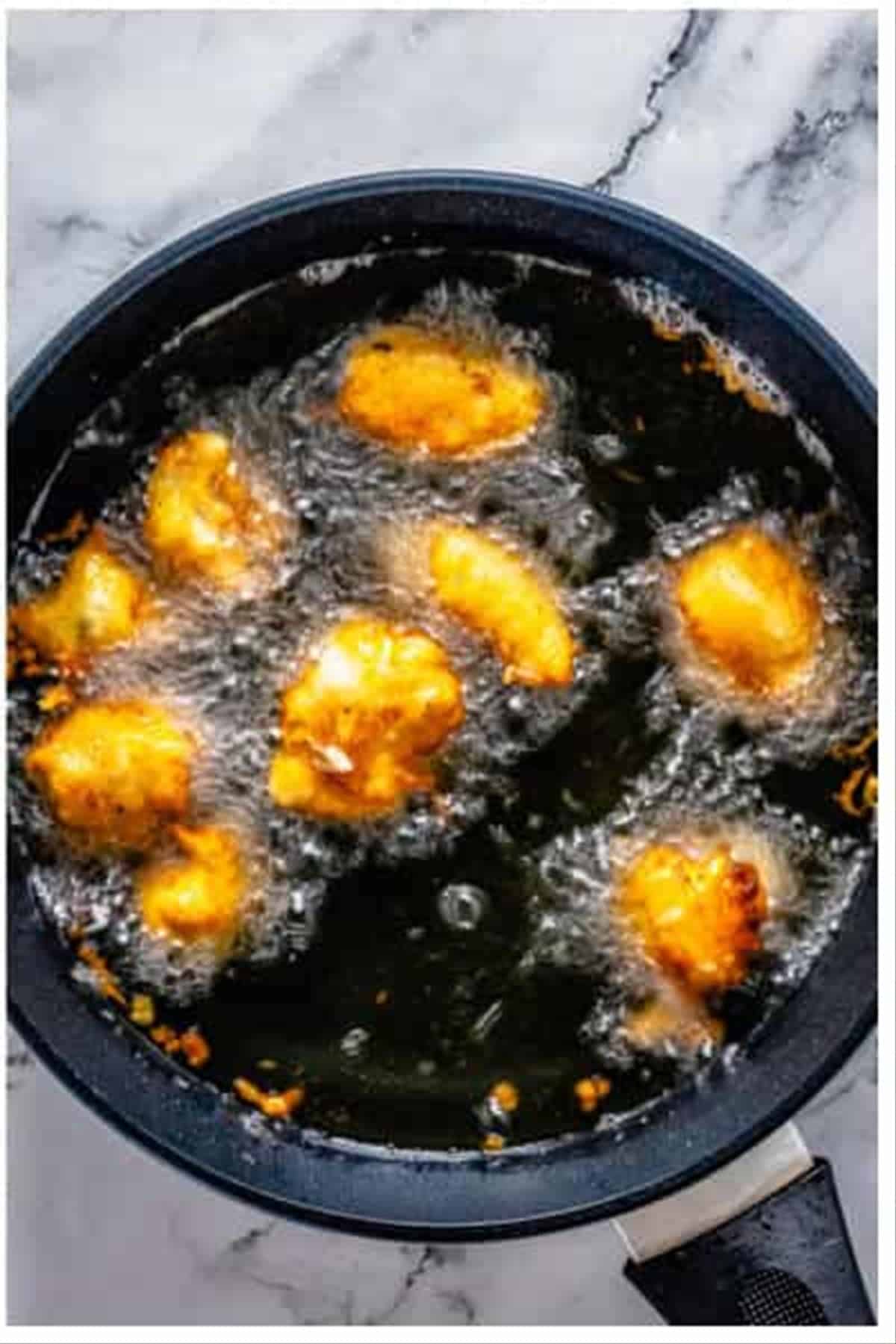 Battered chicken pieces frying to golden brown in hot oil.