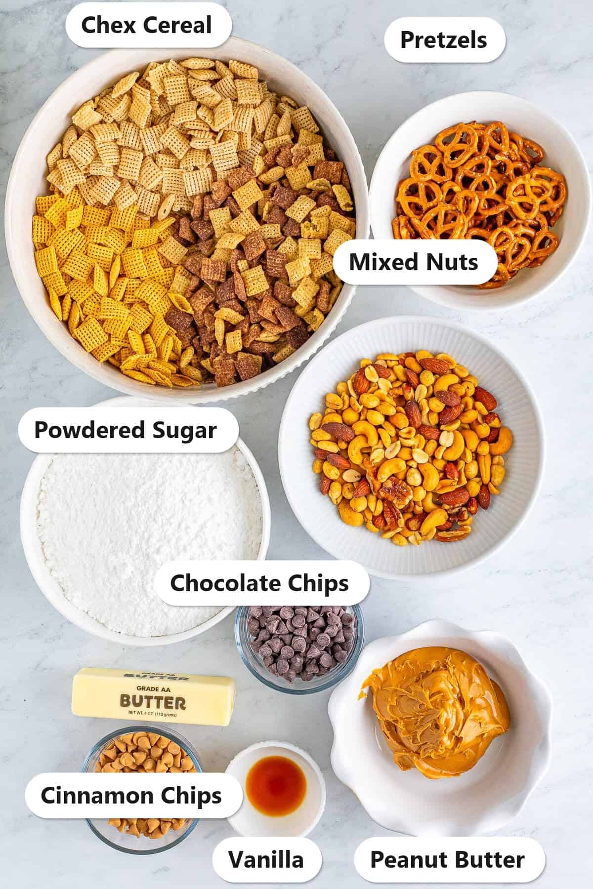 Labeled ingredients flat lay showing Chex Cereal, Pretzels, Mixed Nuts, Powdered Sugar, Chocolate Chips, Peanut Butter, Cinnamon Chips, and Vanilla for the Best Sweet Chex Mix Recipe Muddy Buddy.