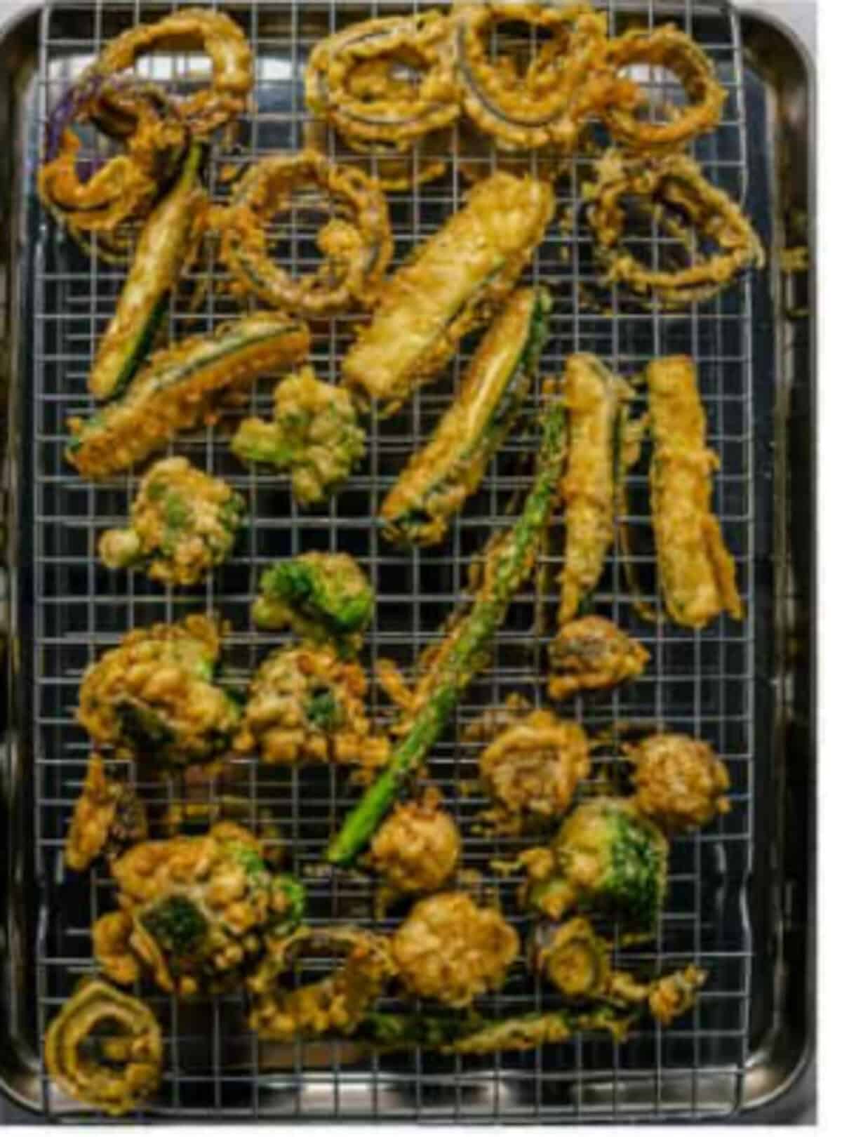 Crispy Tempura Vegetables Recipe drained on a wire rack over a sheet tray to prevent soggy bottoms, then served immediately with the soy-based dipping sauce on the side.