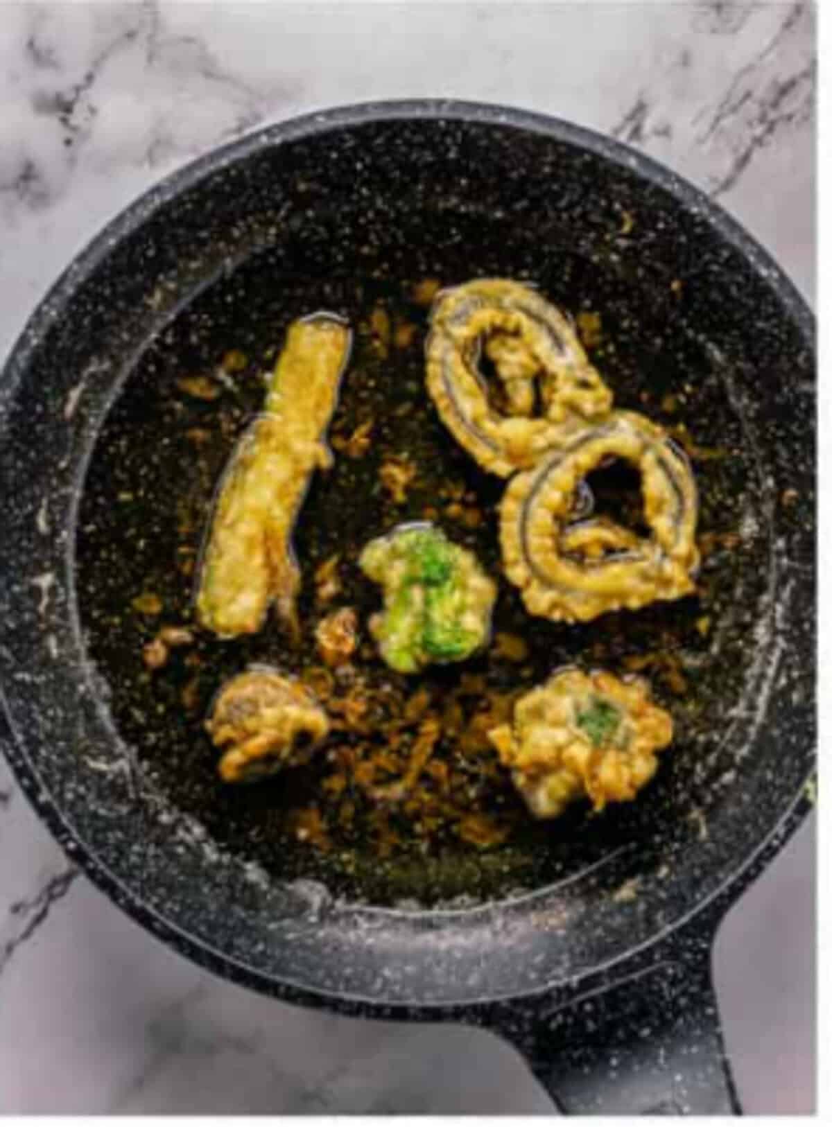 Battered vegetable pieces frying in 350-degree oil until lightly golden brown, the critical step that gives tempura its crispy light texture in the Crispy Tempura Vegetables Recipe.