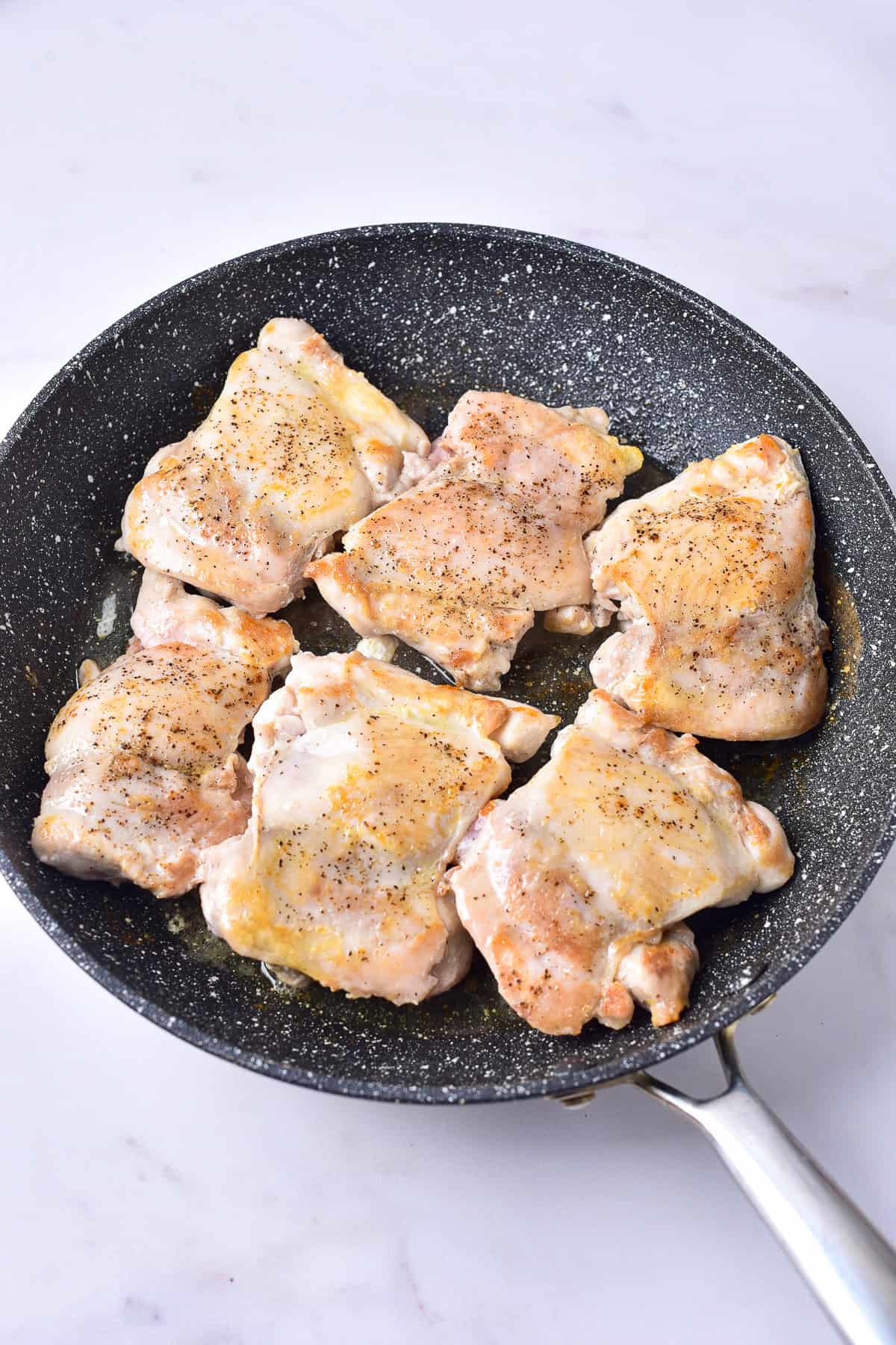 Six chicken thighs seasoned with salt and pepper searing in a large gray skillet for Panda Express Teriyaki Chicken Recipe.