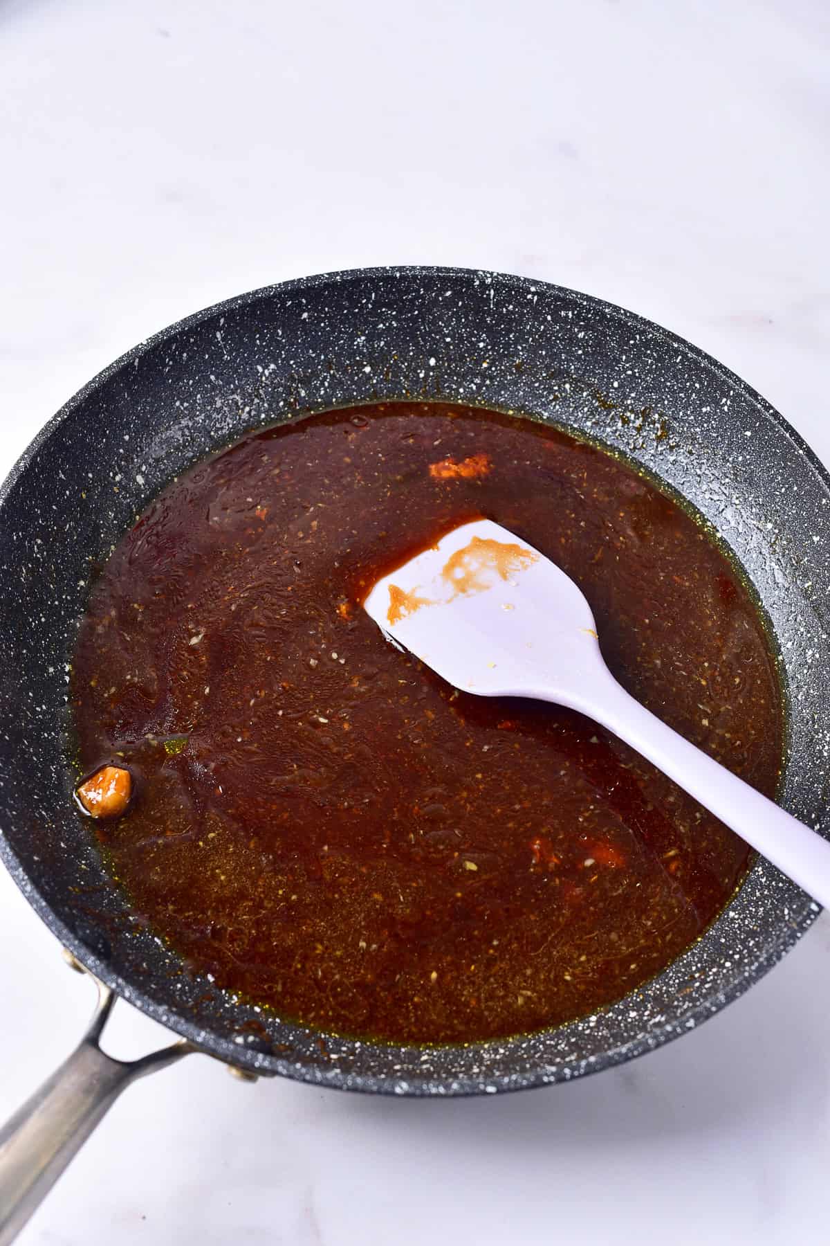 Teriyaki sauce simmering and thickening in a gray skillet with a white spatula for Panda Express Teriyaki Chicken Recipe.