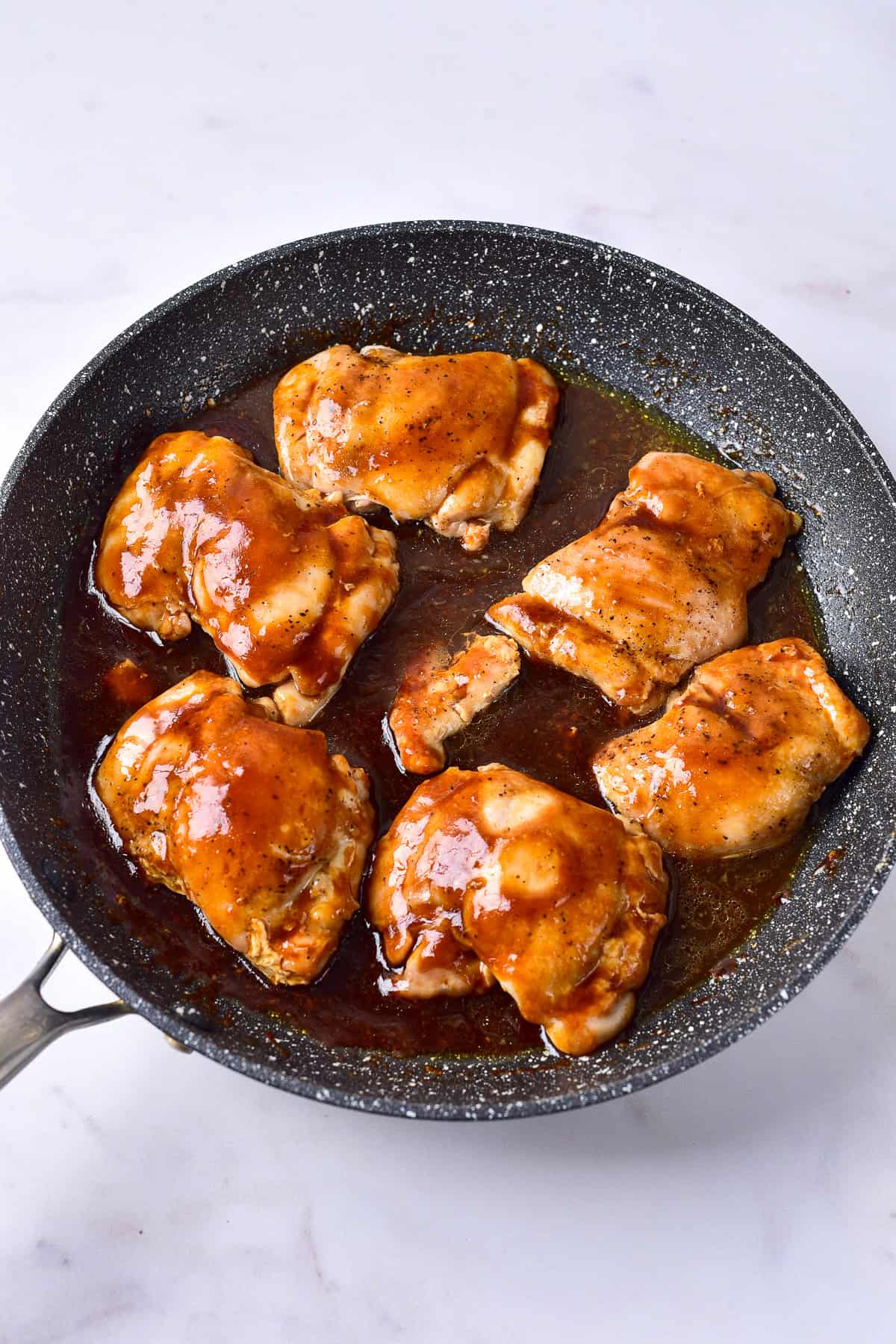 Six chicken thighs coated in glossy teriyaki glaze in a gray skillet for Panda Express Teriyaki Chicken Recipe.