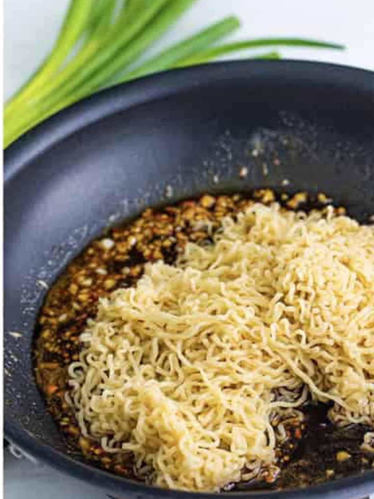 Adding cooked ramen noodles to the sauce in the skillet.