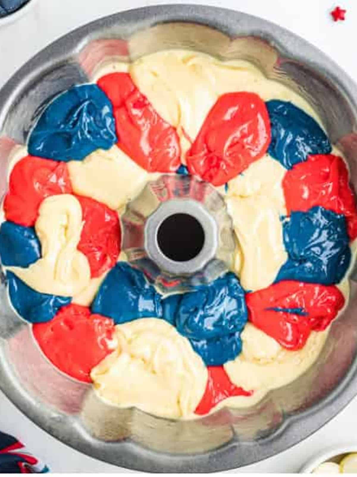 Red, white, and blue batter spooned into a bundt pan for a 4th of July Cake.