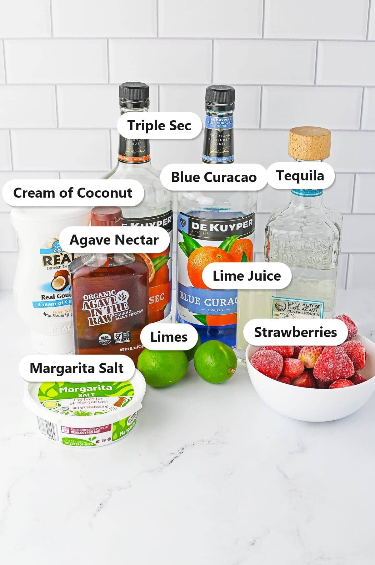 Labeled ingredients for 4th of July cocktails including tequila, triple sec, blue curacao, cream of coconut, agave, lime juice, limes, strawberries, and margarita salt.