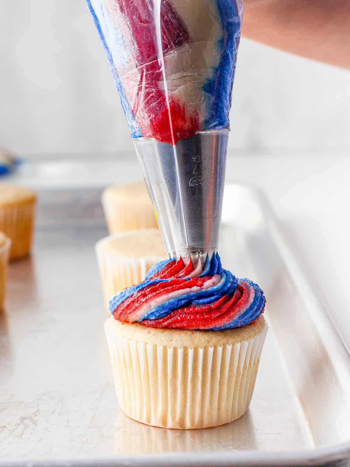 Piping a patriotic red, white, and blue swirl onto a 4th of July cupcake.