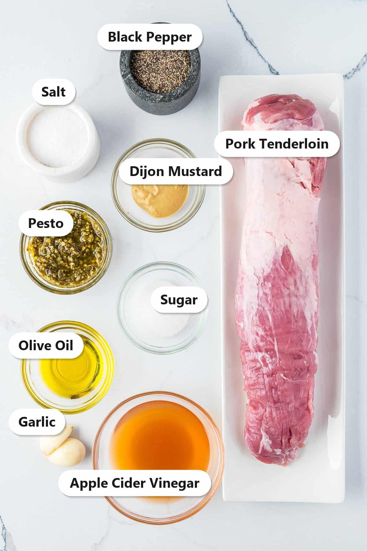 Labeled ingredients for grilled pork tenderloin including pork tenderloin, pesto, apple cider vinegar, Dijon mustard, garlic, olive oil, sugar, salt, and black pepper.